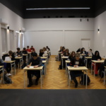 sala z czterema rzędami pojedynczych stolików, przy których uczniowie piszą test