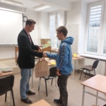 Uczeń odbiera torbę z nagrodą z rąk nauczyciela